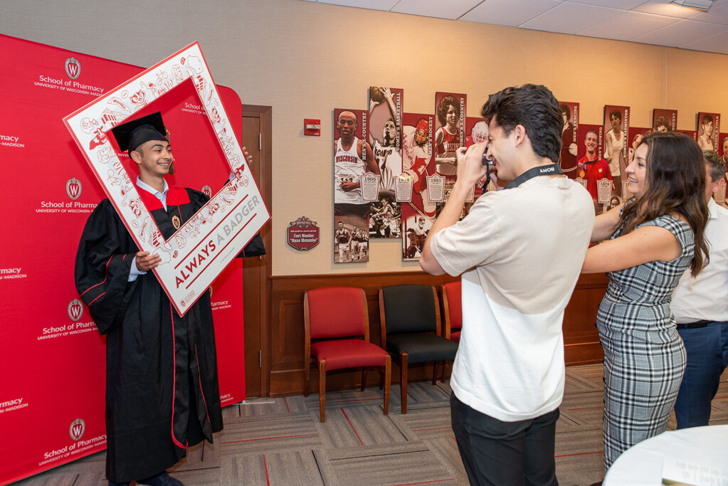 Graduated student standing in front of a red backdrop using frame prop