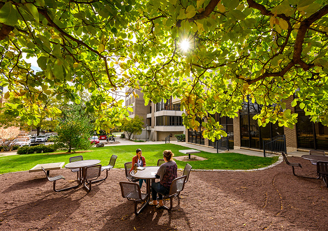 Two students sit at a table in a lush garden area