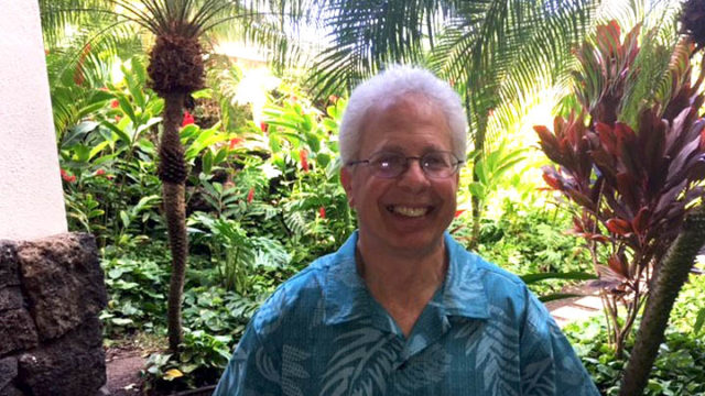 Bob Breslow stands smiling in front of lush, green vegetation