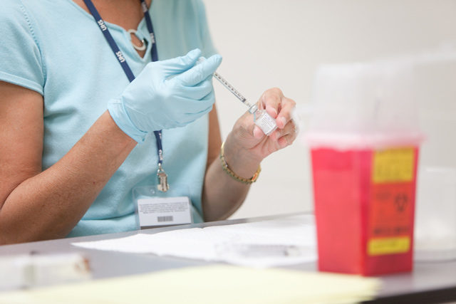 Nurse wearing glove extracting liquid from vial with syringe