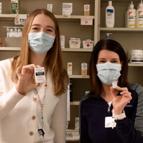 Anna Lattos and Kate Cain holding vials of COVID vaccine