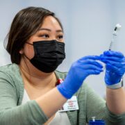 Phanary Xiong, wearing a mask and blue gloves, holds a vaccine needle