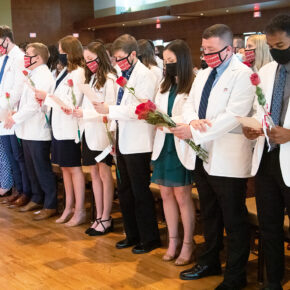 Pharm students holding roses and white coat ceremony pamphlets