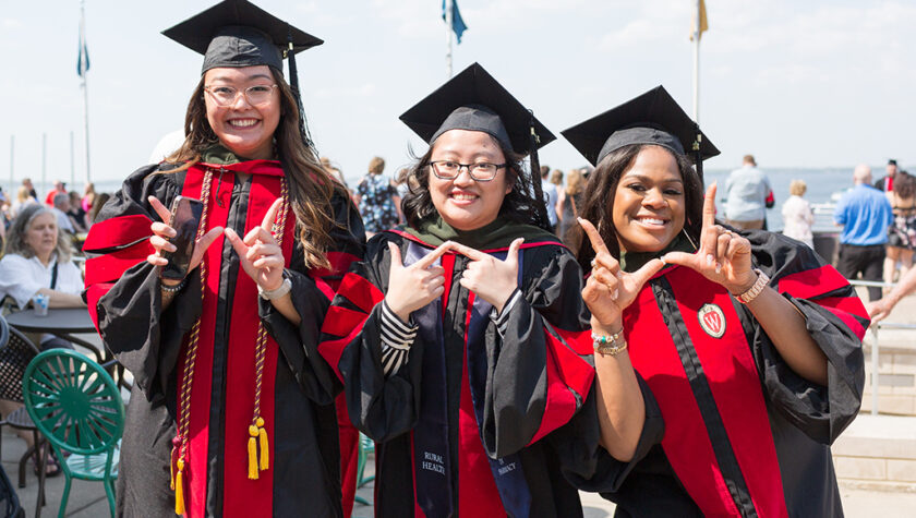 PharmD graduates Lorewell Buaya, Kathy Chao, and Silvya Velez Pache pose together with W hand gestures at Memorial Union Terrace following the 2022 Hooding Ceremony.