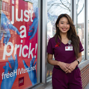 ThuyVu Do stands near a "just a prick" sign to encourage HIV testing.