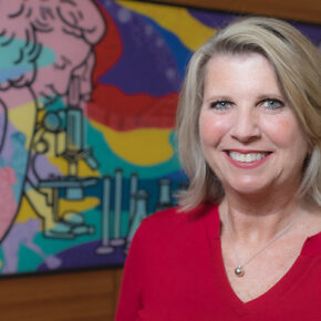 A portrait of Debra Fluno in front of a colorful mural