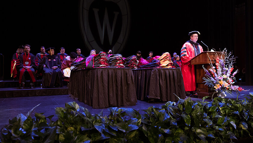 Dean Steve Swanson onstage, speaking at a podium in graduation robes