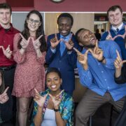 Students together in a large dining room, using their hands to form a "W" for the camera