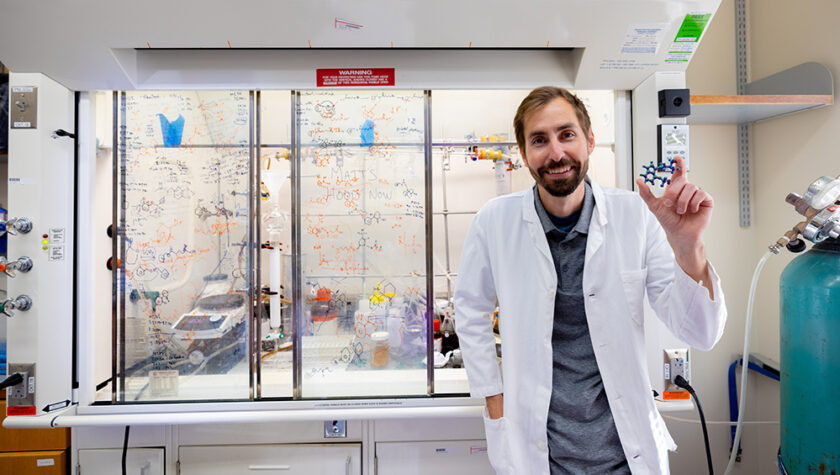 Cody Wenthur holding up a molecule model in his lab and smiling