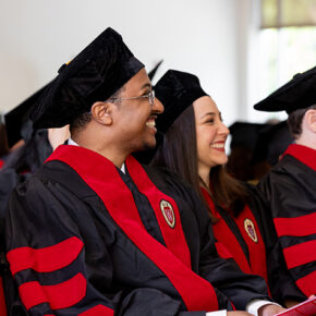 School of Pharmacy graduates in hats and robes smile while listening to a speaker.