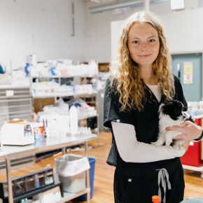 Sydney Wiese in scrubs, holding a small dog.