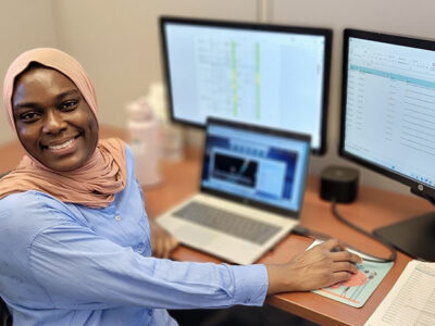 Fatima Abdul Rasheed at a desk working with computers and smiling