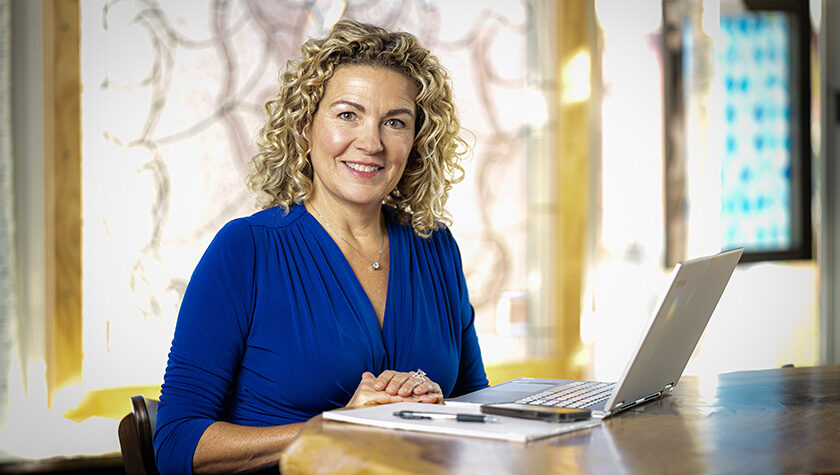 Lani Bertrand smiles while seated at a table in front of a laptop.