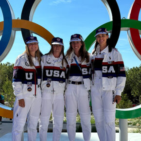 Four women in "USA" gear posing in front of the Olympic rings.