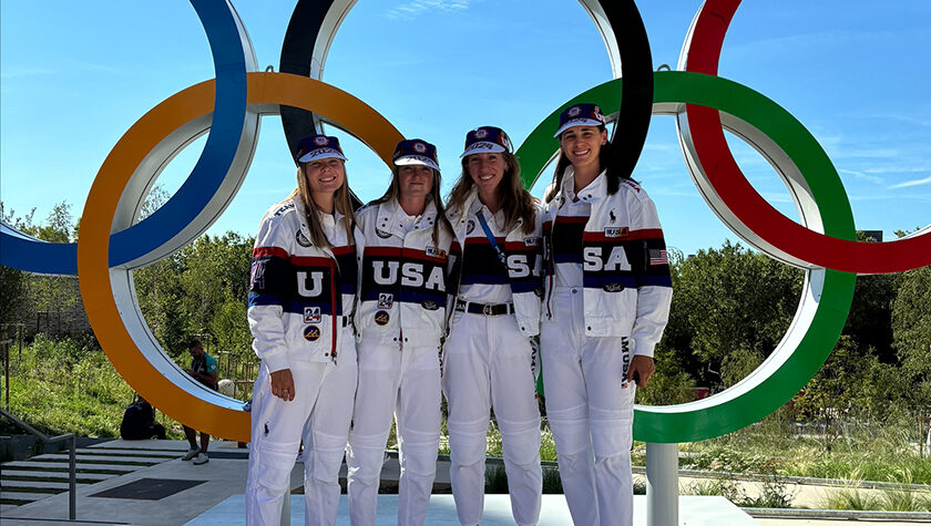 Four women in "USA" gear posing in front of the Olympic rings.