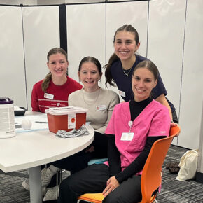 PharmD students Amalia Fox, Hannah Whitney, Chaise Pucek, and Nicole Ulbricht pose behind a white folding table with vaccination supplies on it.