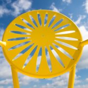 A yellow Memorial Union Terrace chair is pictured against a sunny blue sky at UW-Madison.. The chair is known for its iconic sunburst design. (Photo by Jeff Miller/UW-Madison)