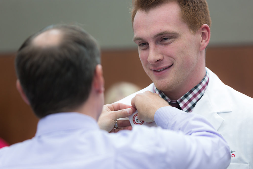 Student accepts pin from Jason Law, alumni of the School.