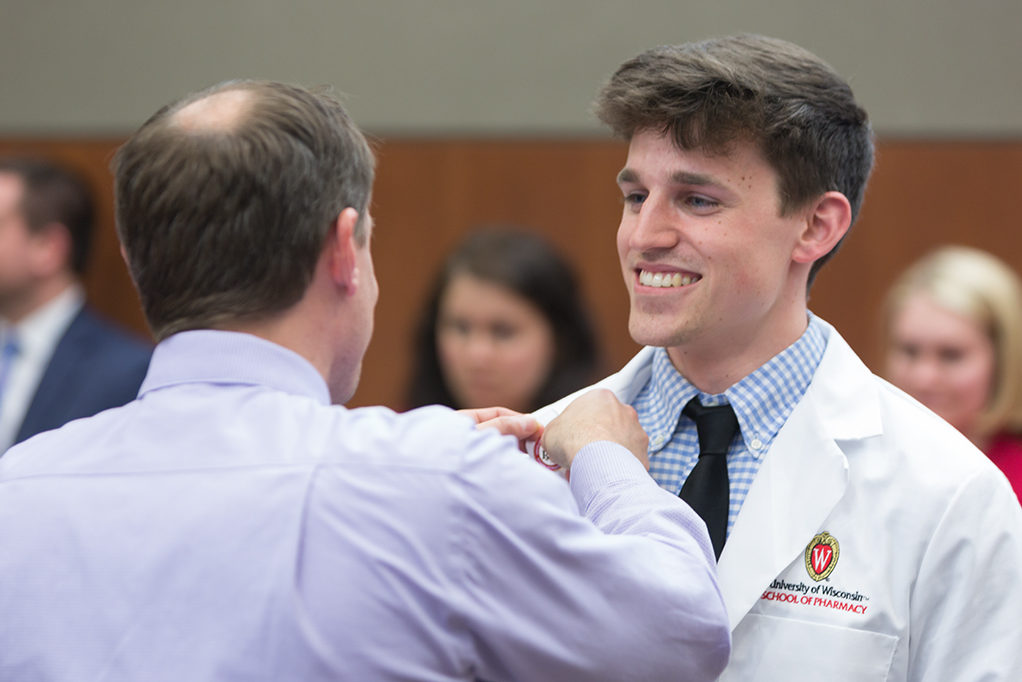 Student accepts pin from Jason Law, alumni of the School.