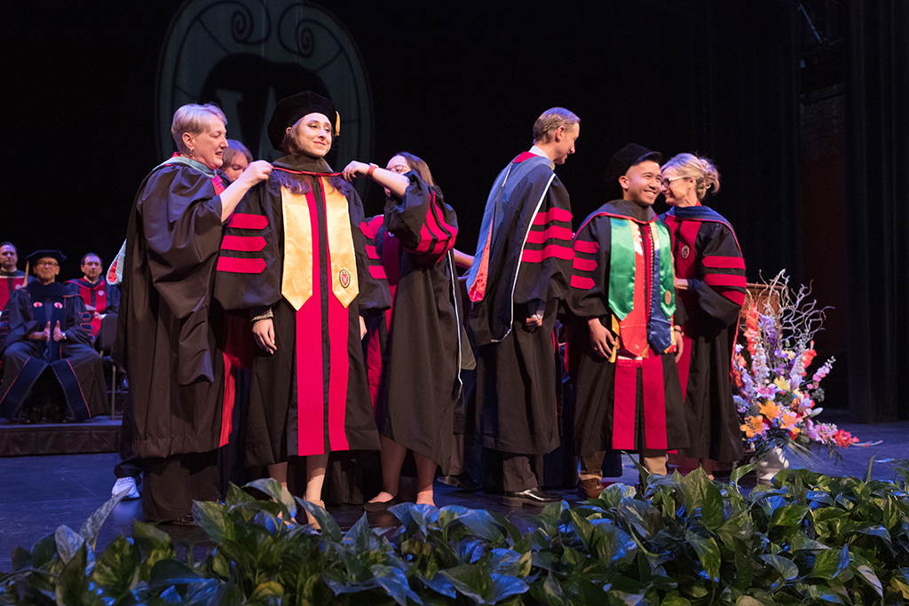 Faculty place a hood over a graduate's head.