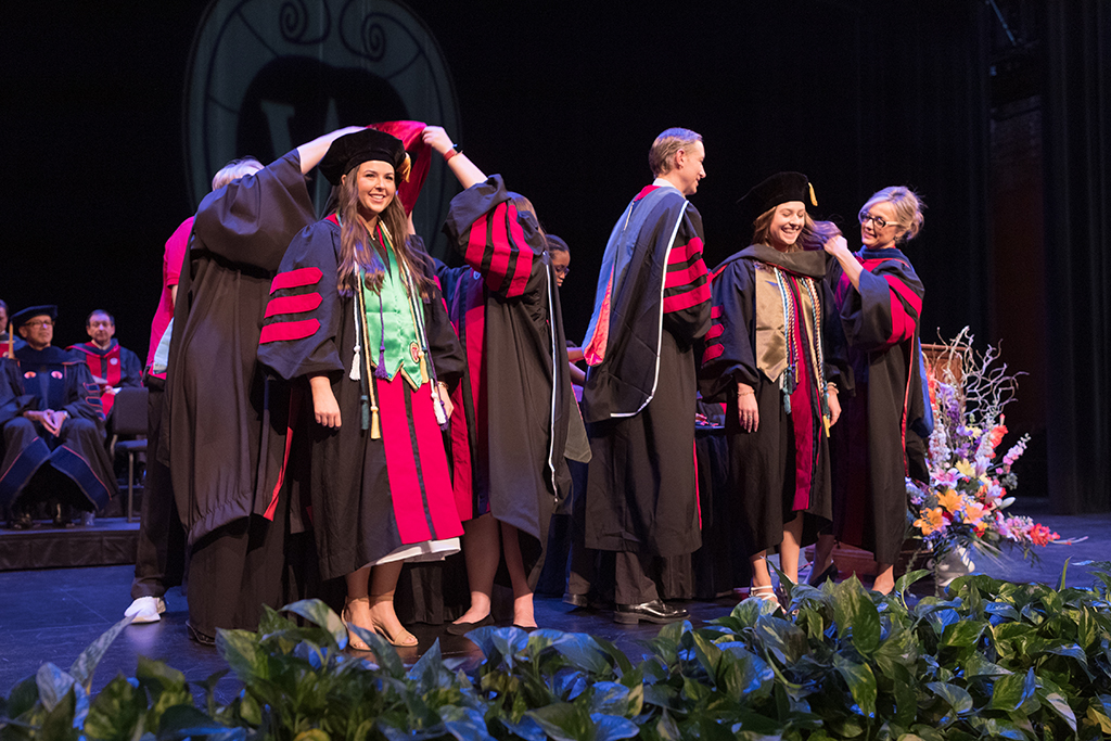 Faculty place a hood over a graduate's head.