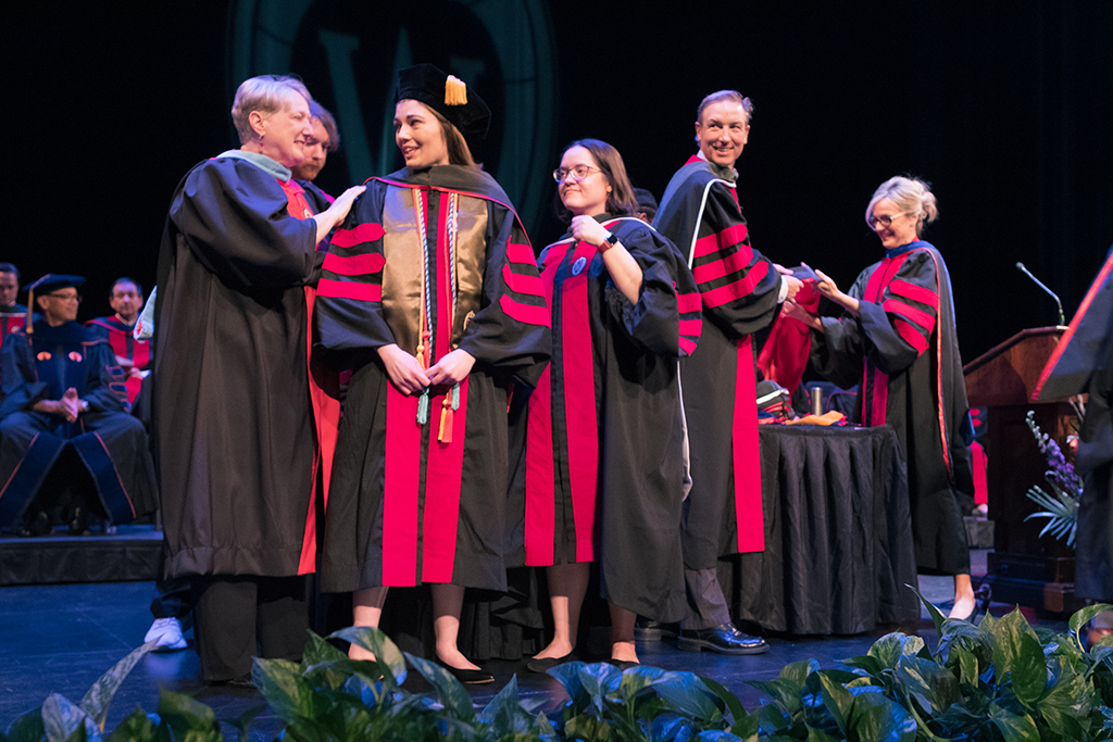 Faculty place a hood over a graduate's head.