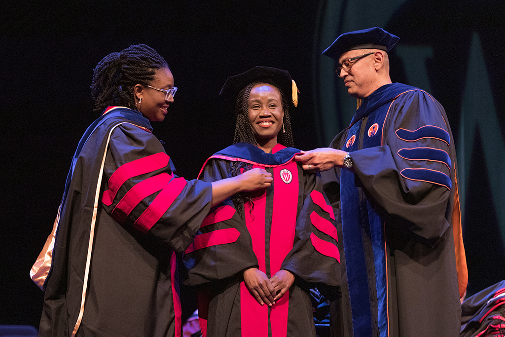 Faculty place a hood over a graduate's head.