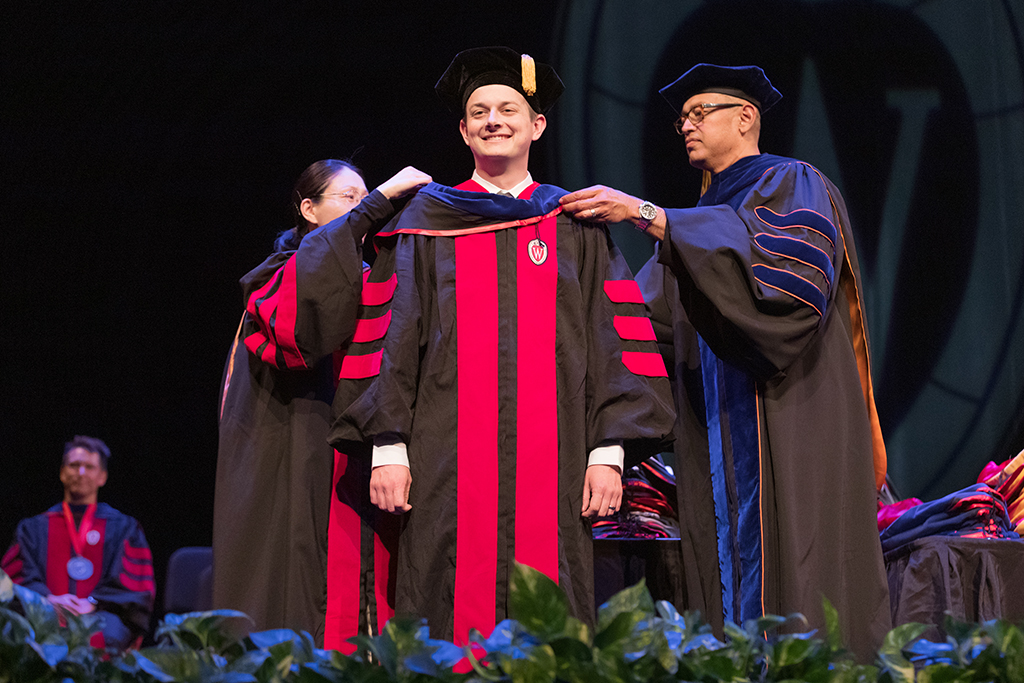 Faculty place a hood over a graduate's head.