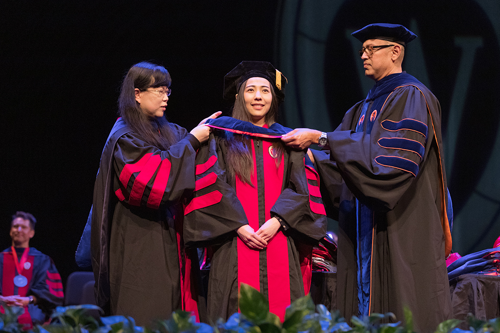Faculty place a hood over a graduate's head.