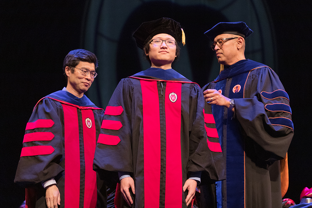 Faculty place a hood over a graduate's head.