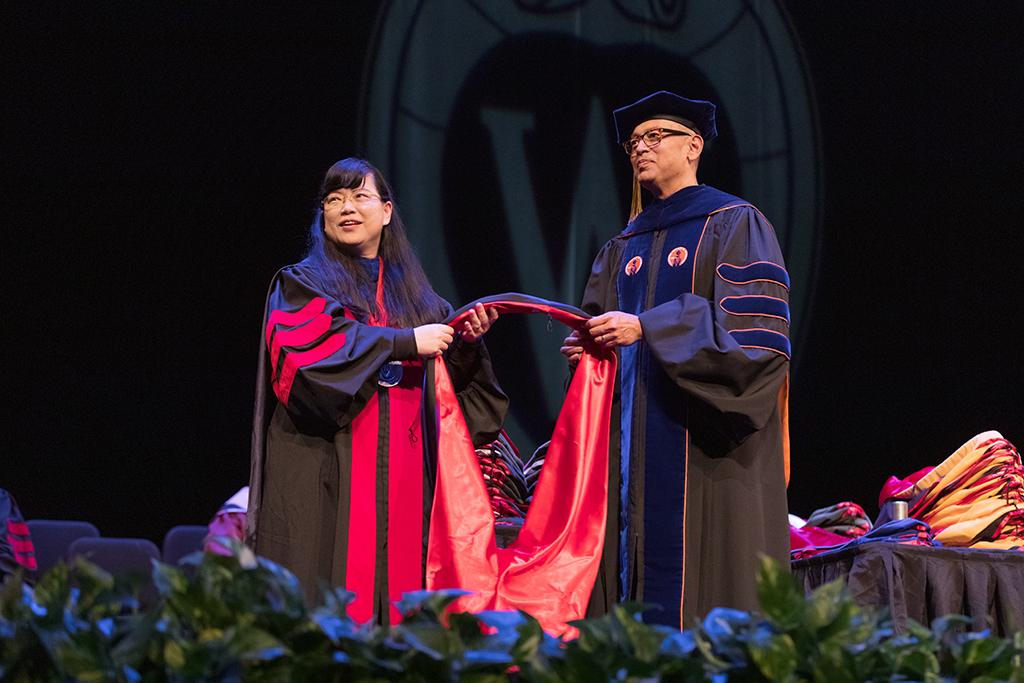 Faculty place a hood over a graduate's head.
