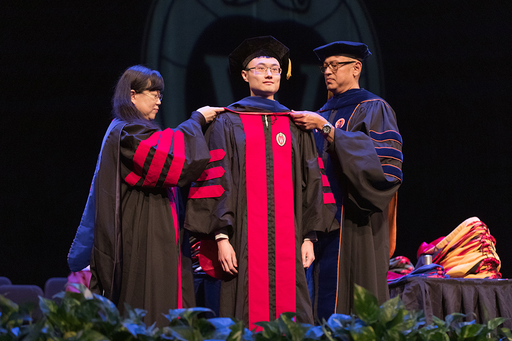 Faculty place a hood over a graduate's head.