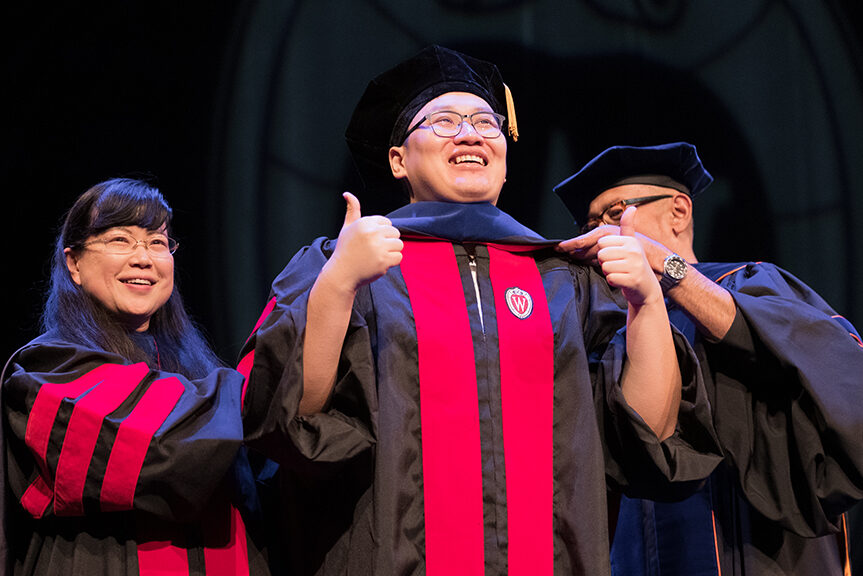 Faculty place a hood over a graduate's head.