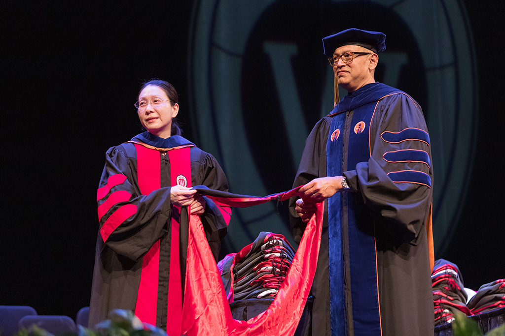Faculty place a hood over a graduate's head.