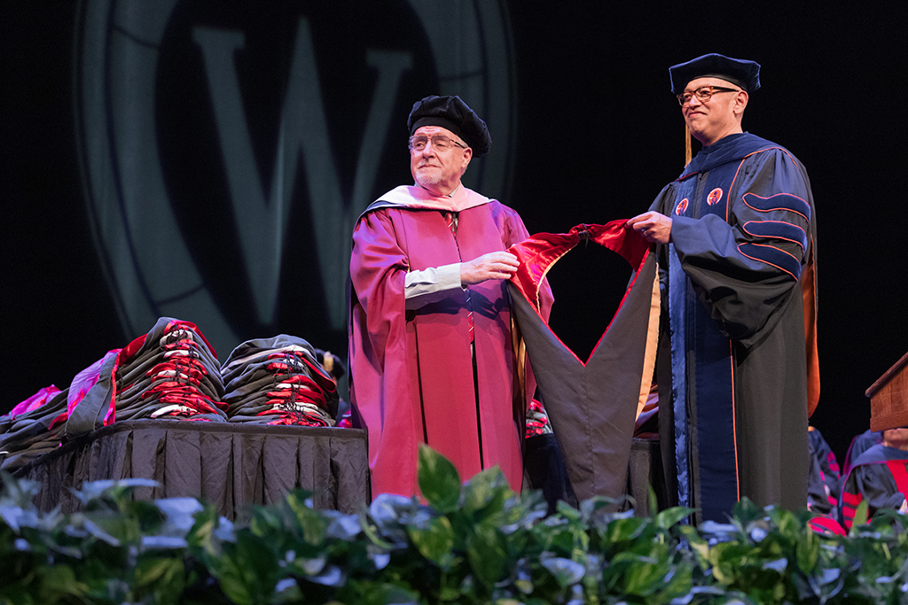 Faculty place a hood over a graduate's head.