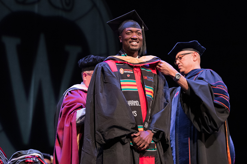 Faculty place a hood over a graduate's head.
