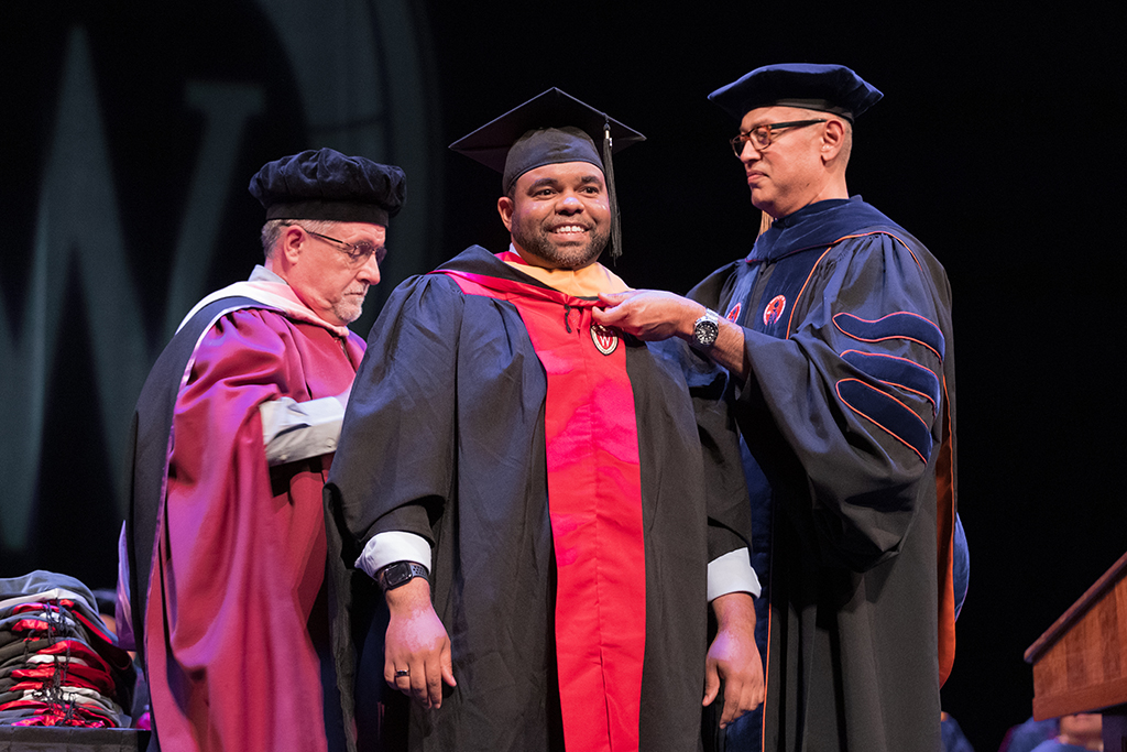 Faculty place a hood over a graduate's head.