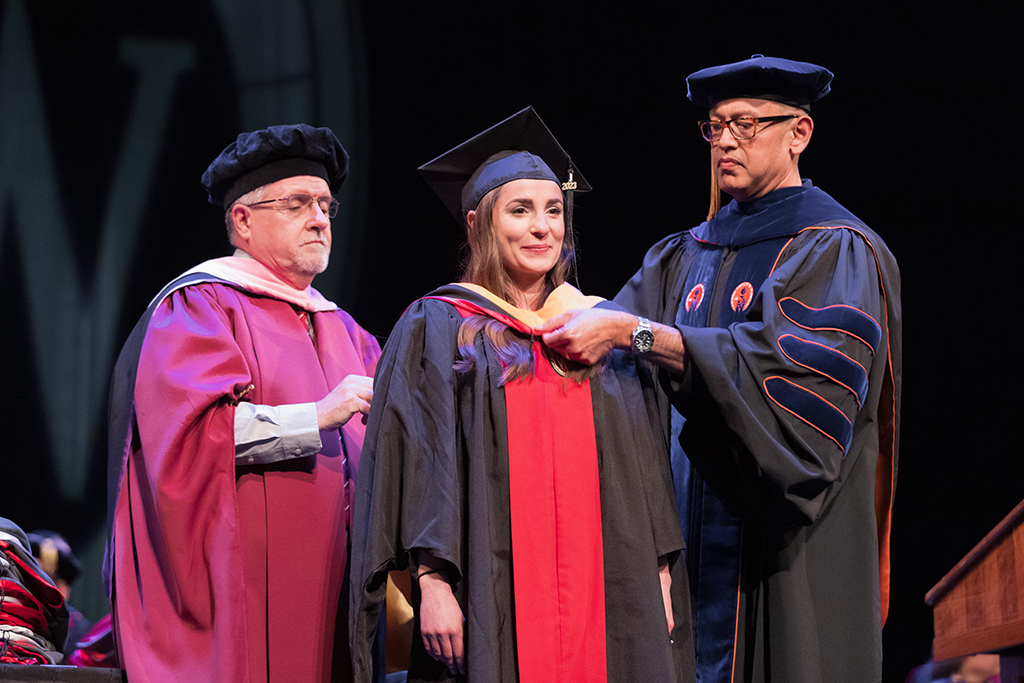 Faculty place a hood over a graduate's head.
