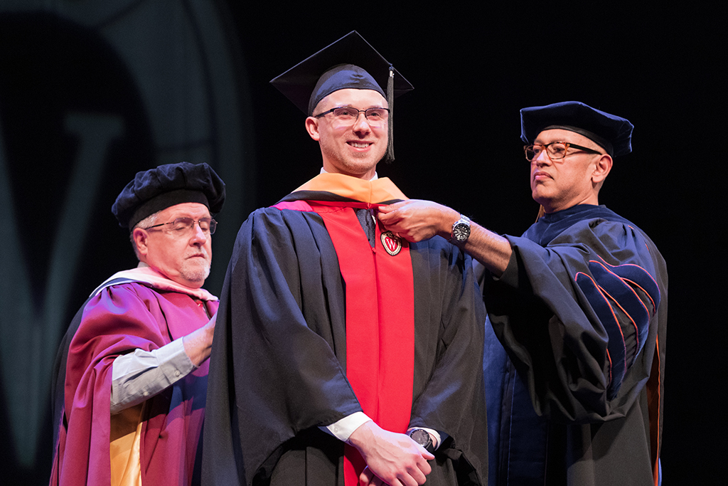 Faculty place a hood over a graduate's head.