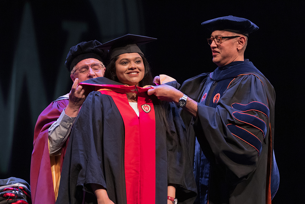 Faculty place a hood over a graduate's head.