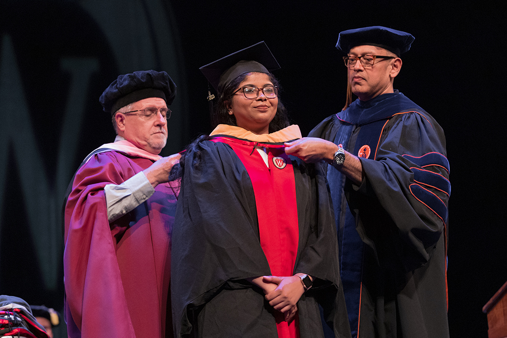 Faculty place a hood over a graduate's head.