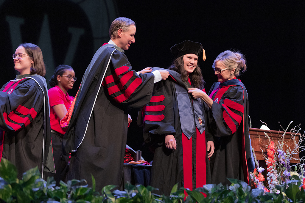 Faculty place a hood over a graduate's head.