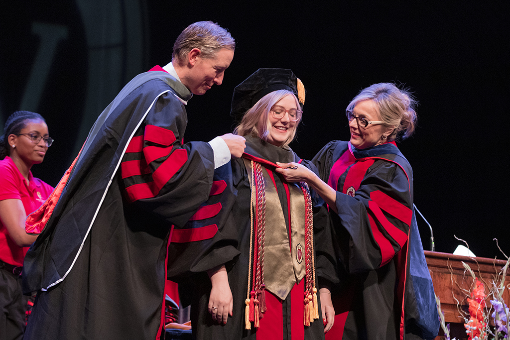 Faculty place a hood over a graduate's head.
