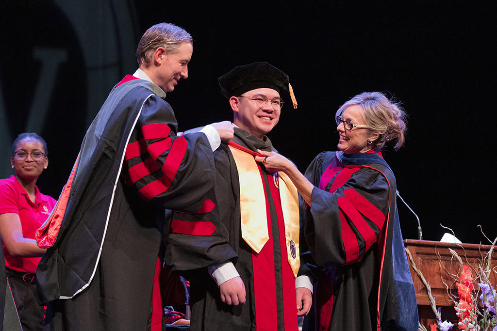 Faculty place a hood over a graduate's head.