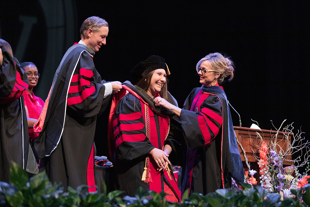 Faculty place a hood over a graduate's head.