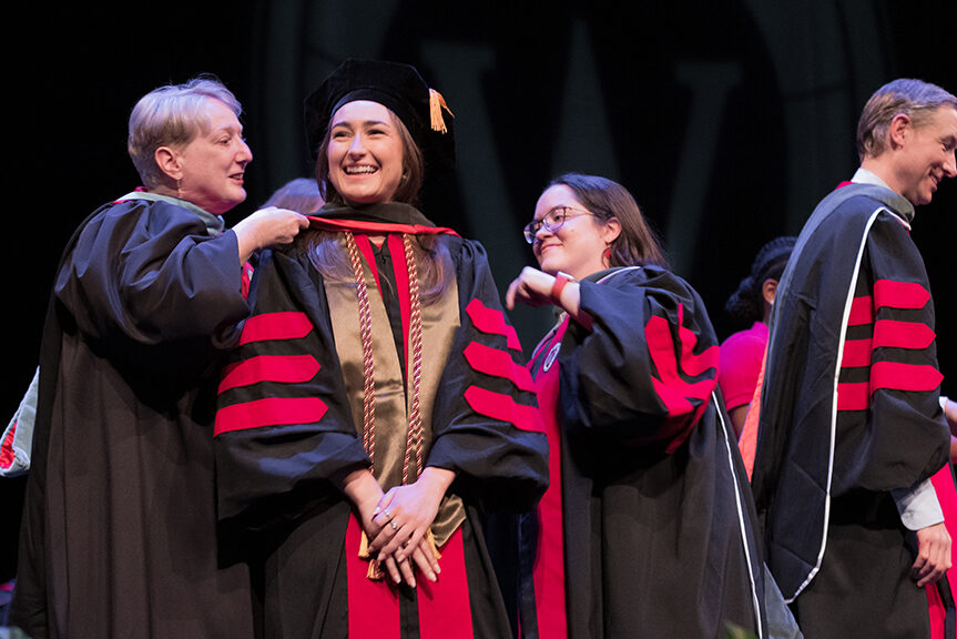 Faculty place a hood over a graduate's head.