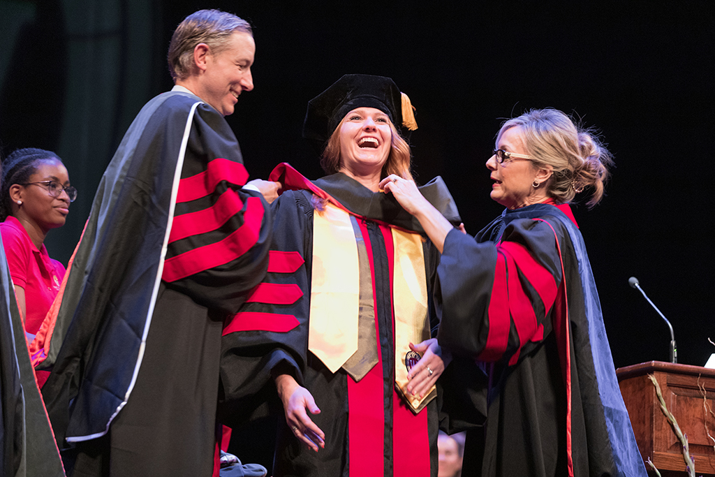 Faculty place a hood over a graduate's head.