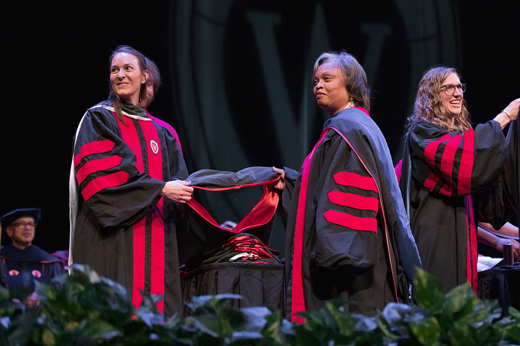 Faculty place a hood over a graduate's head.
