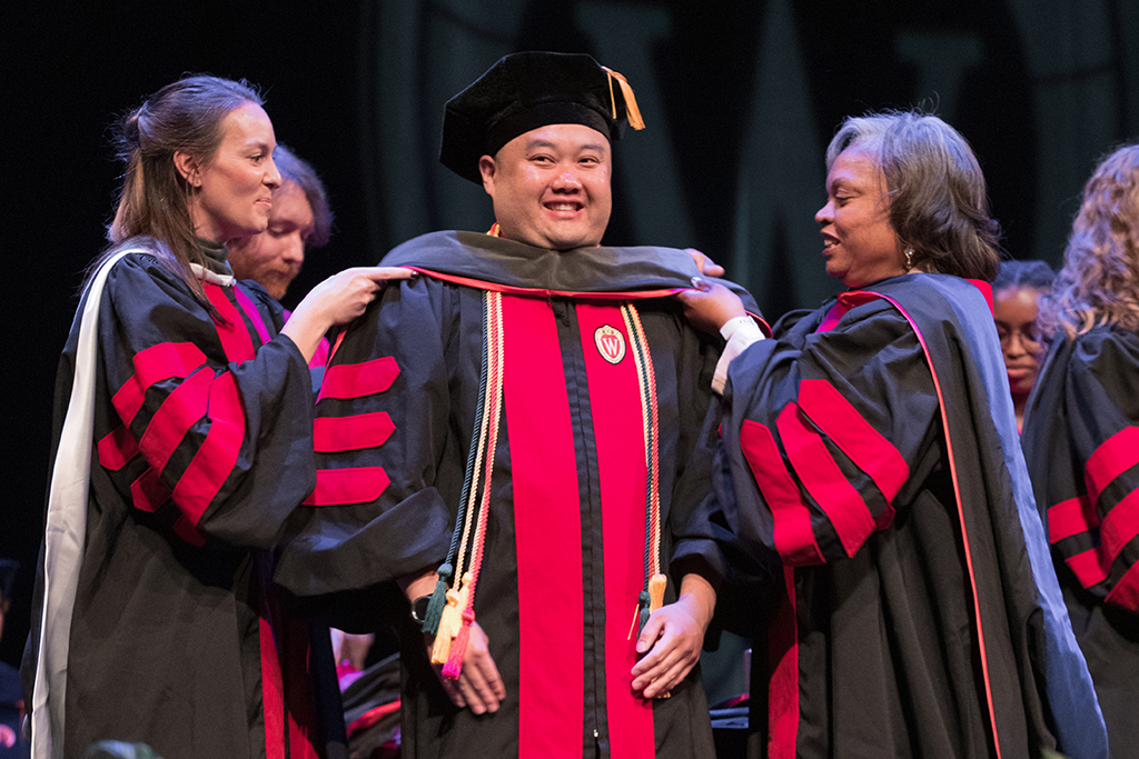 Faculty place a hood over a graduate's head.