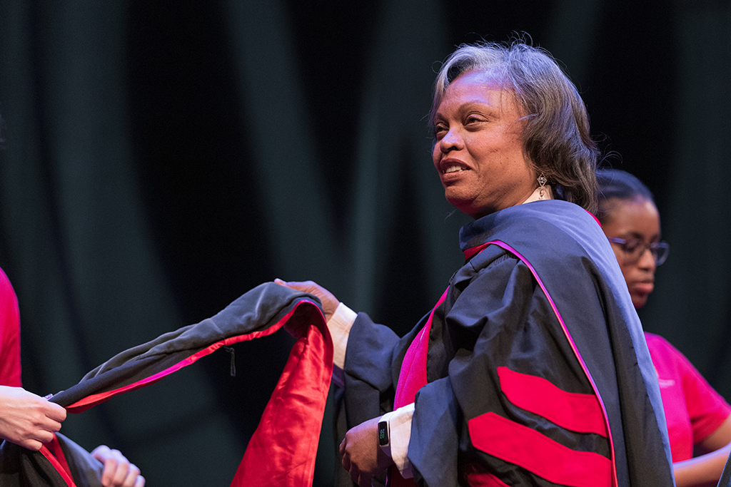Faculty place a hood over a graduate's head.